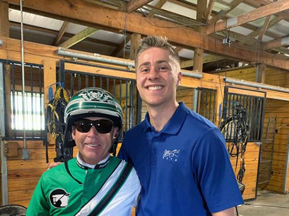 Alex Sausville stand in a barn next to trainer Jimmy Takter